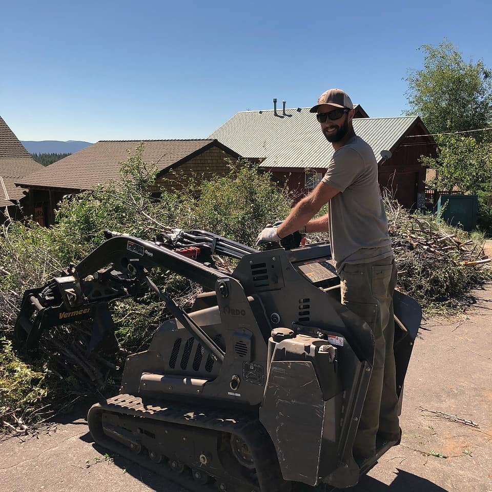 A Kosich crew member on a tracked loader beside a brush pile