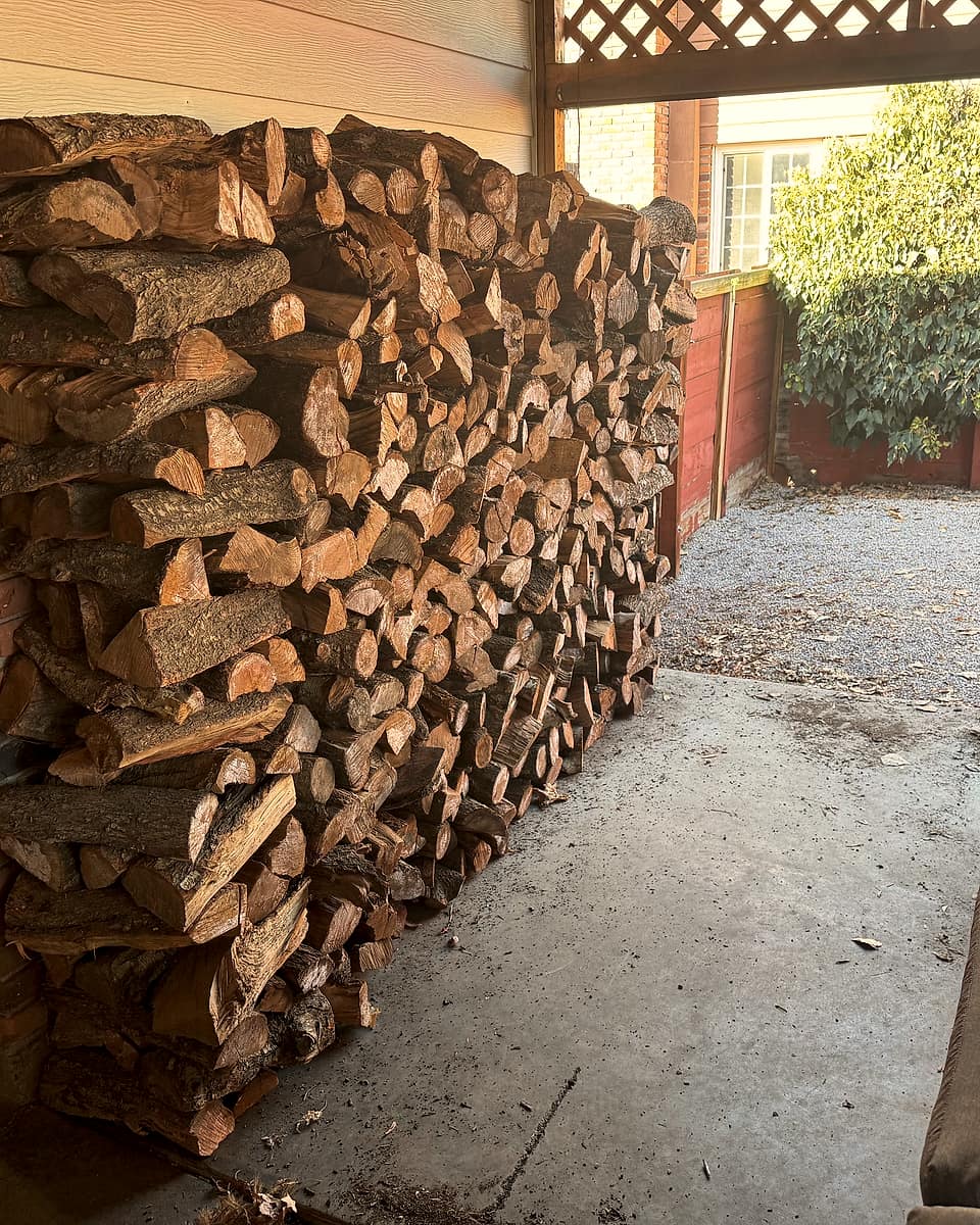 A delivered order of split firewood stacked neatly under a covered patio